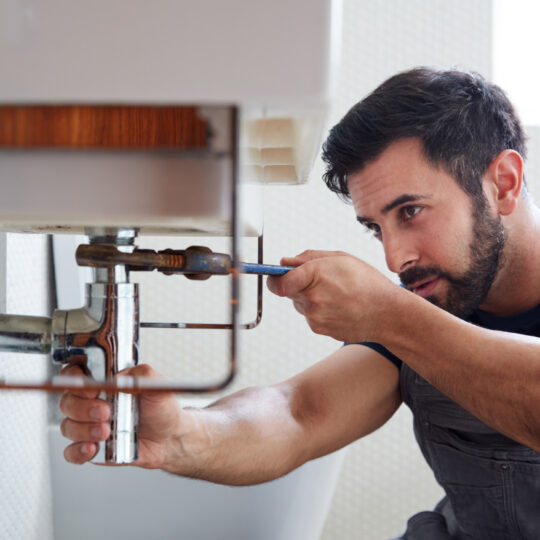 Photo of tradesman fixing a pipe.